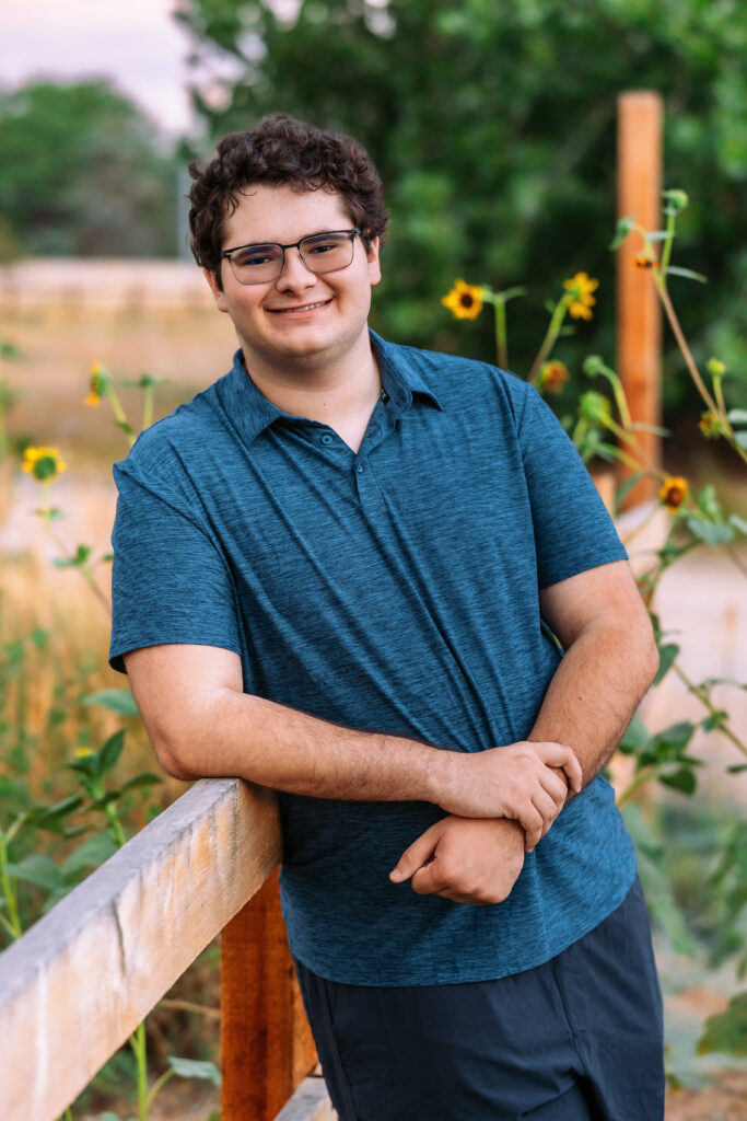 Outdoor senior photo of high school boy with sunflowers in the background, wearing a blue shirt for a session requested by his mom, photographed by Heather Lilly Photography