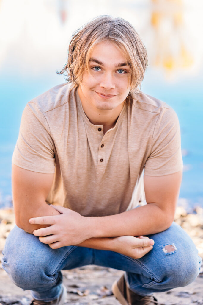 Senior portrait of high school guy showing off arm muscles in front of a bold blue water background, photographed by Northern Colorado senior photographer Heather Lilly