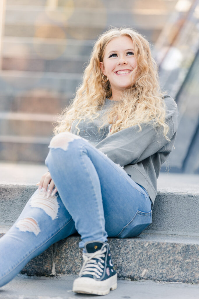 Senior portrait of a teen girl with curly blonde hair, smiling softly in golden light, photographed by Northern Colorado senior photographer Heather Lilly