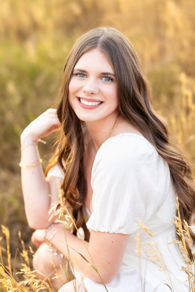 Dreamy senior photo of a brunette girl in a white dress with cascading hair, photographed outdoors during golden hour by Heather Lilly Photography