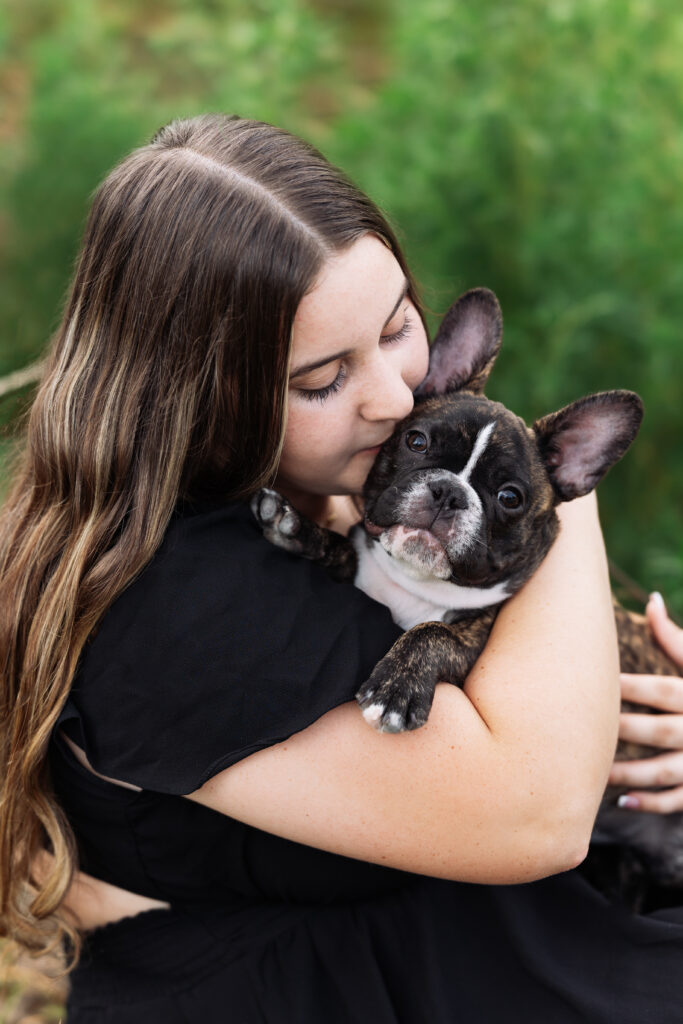 Senior portrait of a teen girl kissing her French Bulldog puppy, captured outdoors in natural light by Northern Colorado senior photographer Heather Lilly