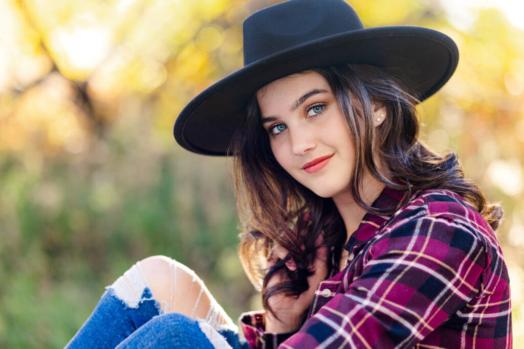 Editorial senior portrait of a teen girl in a black hat and flannel shirt, photographed outdoors in soft natural light by Northern Colorado senior photographer Heather Lilly
