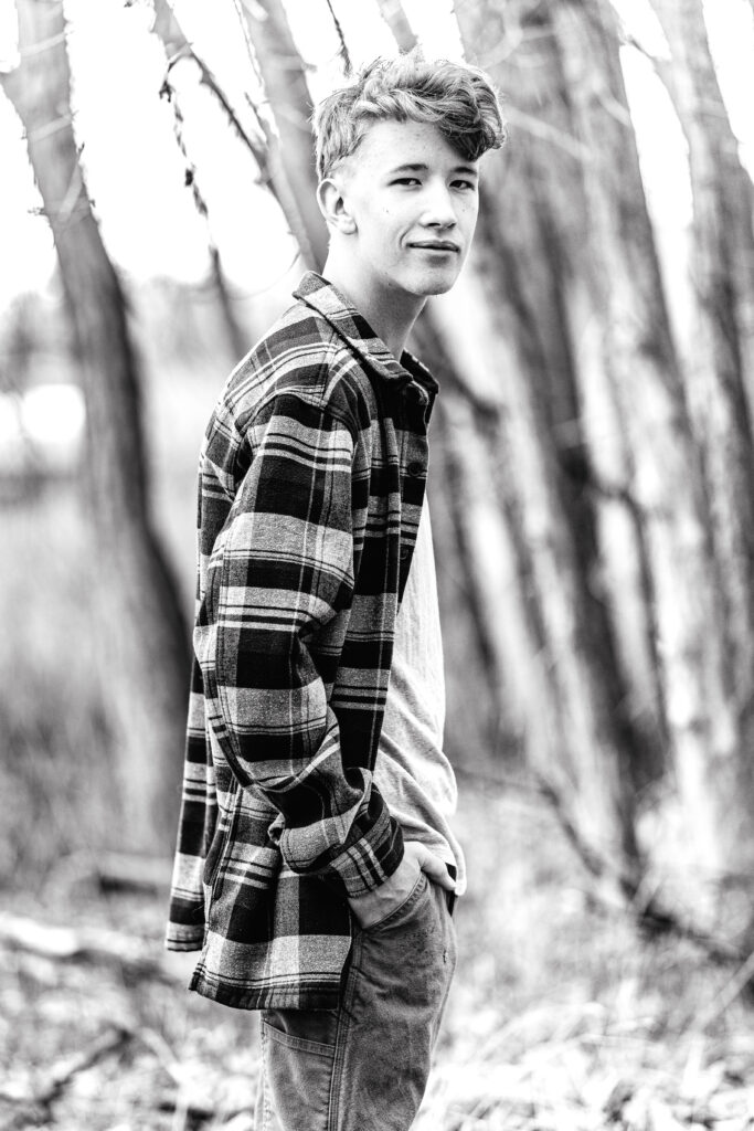 Black and white senior portrait of a teen guy with serious expression and soft bokeh background, editorial lighting and texture, taken by Northern Colorado senior photographer Heather Lilly
