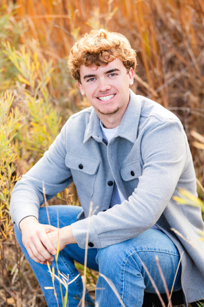 Senior portrait of a teen guy with curly hair and a grey jacket, photographed outdoors in autumn by Northern Colorado senior photographer Heather Lilly