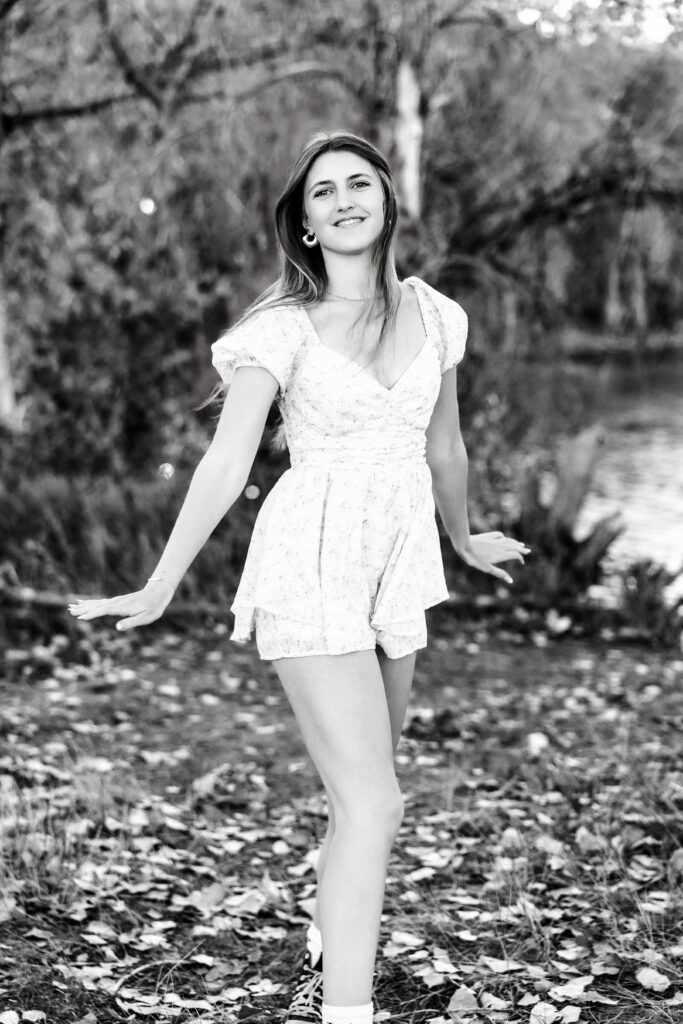 Black and white senior portrait in Greeley CO of a high school girl dancing by a lake, joyful and natural in movement.