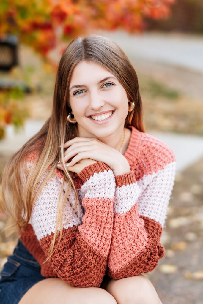 Senior portrait of a teen girl in a pink striped sweater surrounded by golden autumn leaves, captured by Northern Colorado senior photographer Heather Lilly