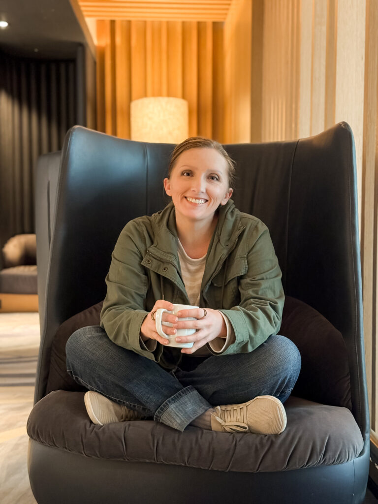 Heather Lilly sitting in an airport lounge chair with coffee in hand on her way to a photography conference, reflecting her role as a creative entrepreneur and blog writer