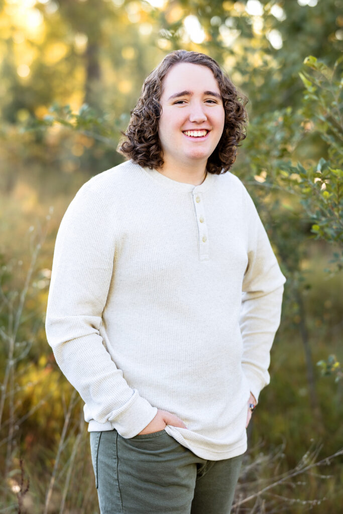 Smiling senior portrait of a teen guy with longer curly hair and soft bokeh background, photographed by Northern Colorado senior photographer Heather Lilly