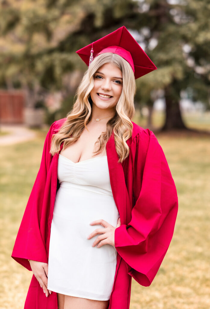 Senior in red gown and white dress at cap and gown portrait session
