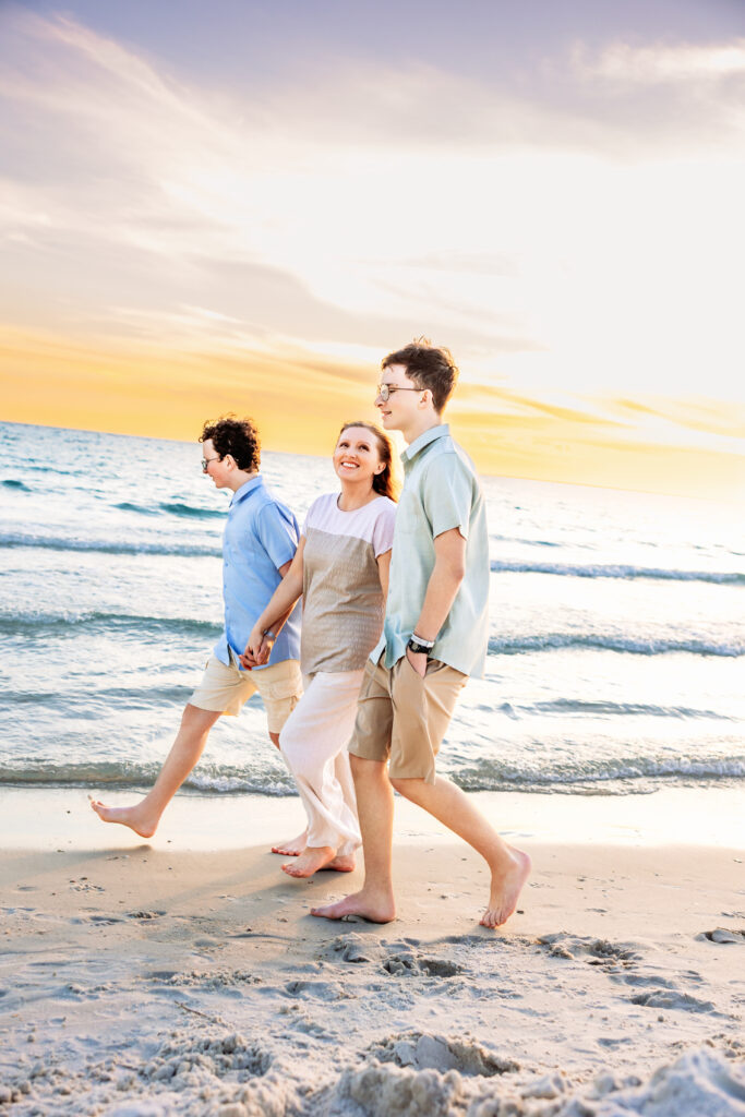 Heather Lilly walking along a Florida beach with her two sons during sunset, surrounded by a soft cotton-candy sky—balancing motherhood, creativity, and entrepreneurship