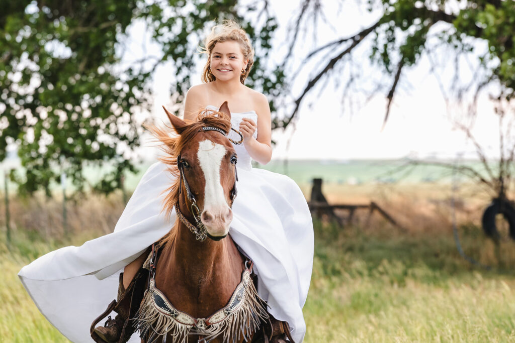 Smiling teen girl in a white wedding dress riding her horse during an equestrian milestone portrait session in Eaton, Colorado with Heather Lilly Photography, LLC