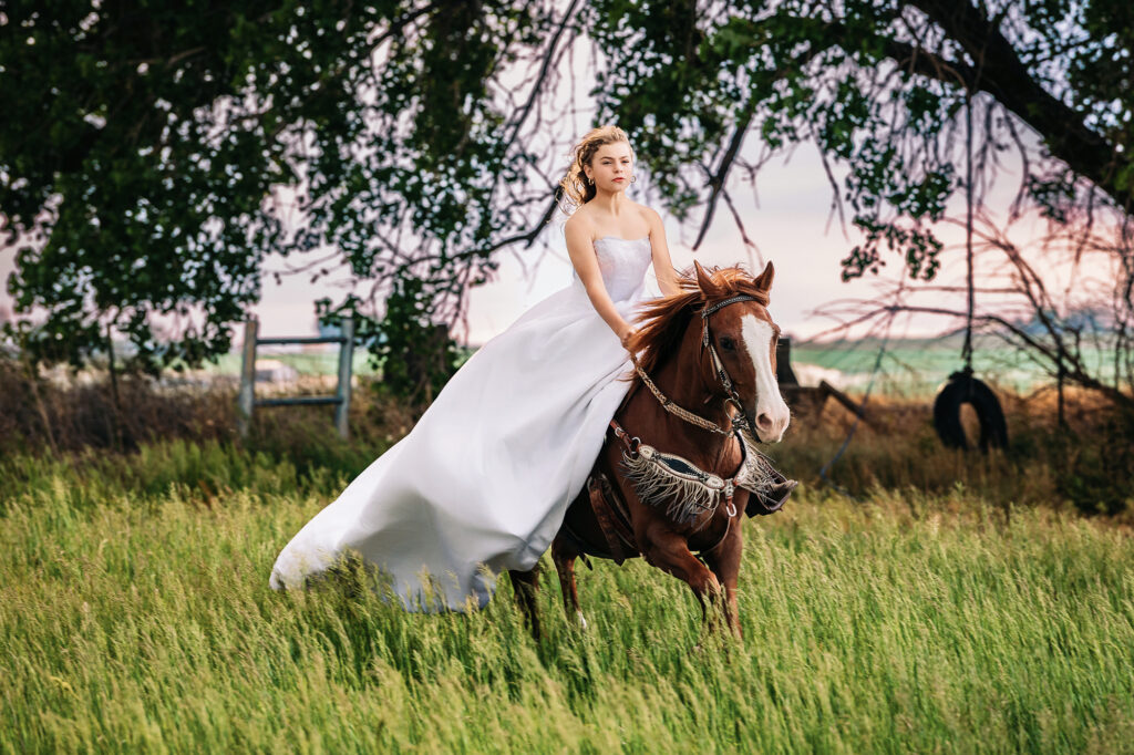 Tween girl in a flowing bridal gown riding a horse through tall grass during a cinematic equestrian portrait session at sunset in Eaton, Colorado, captured by Heather Lilly Photography, LLC


