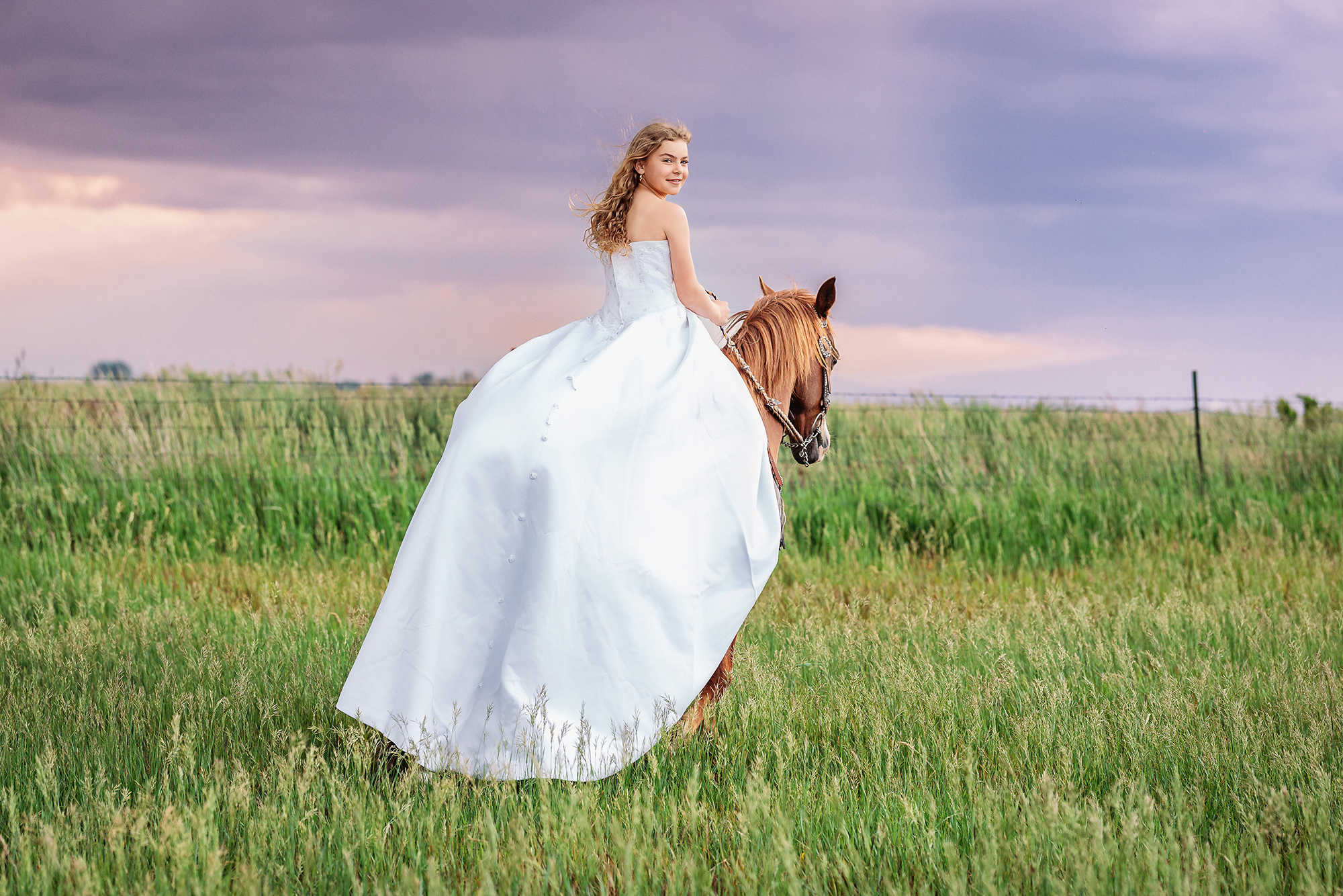 Teen girl riding a horse in her mom’s 2004 wedding dress through a green field in Eaton, Colorado during a moody sunset milestone portrait session