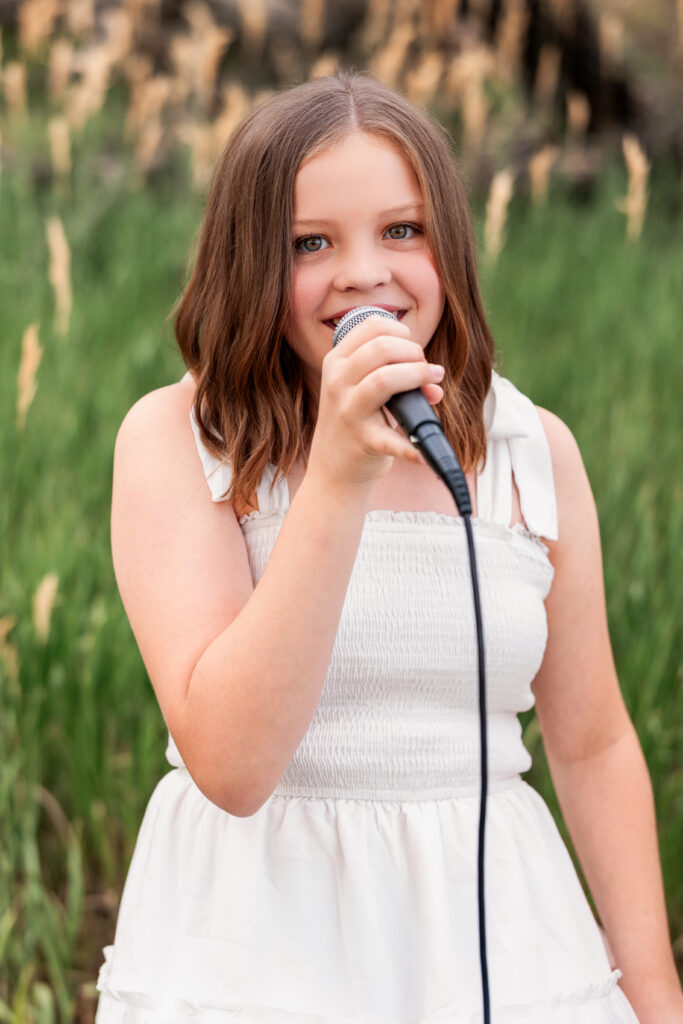 Young girl singing into a microphone in a natural outdoor setting during a Christian country portrait session in Northern Colorado