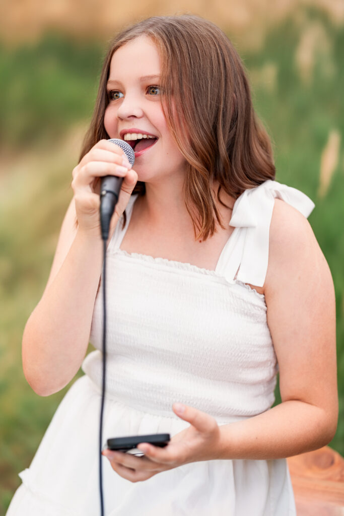 Young girl singing expressively into a microphone in an outdoor setting during a Northern Colorado Christian country portrait session