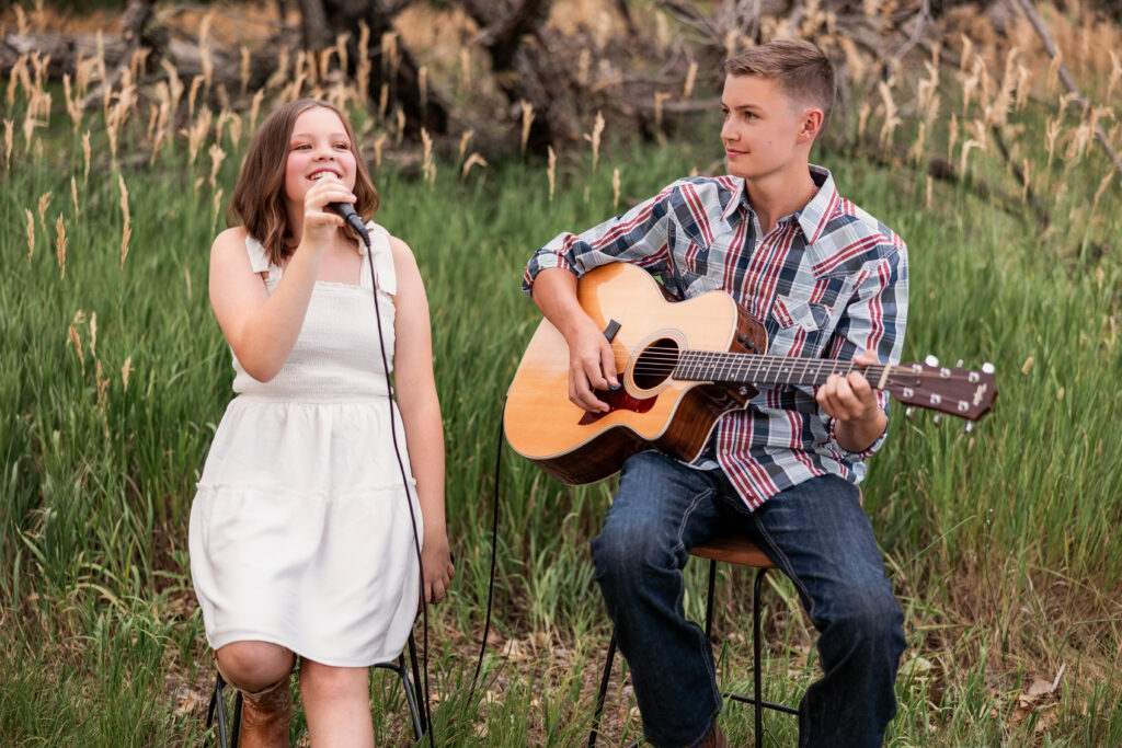 Brother and sister performing together with guitar and microphone in a tall grass field during a country-Christian portrait session in Northern Colorado
