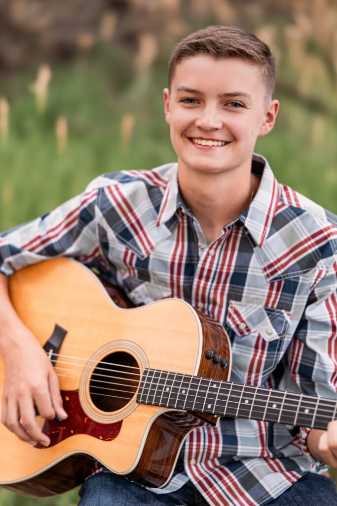 Teenage boy smiling while holding an acoustic guitar during a faith-based editorial portrait session in Northern Colorado