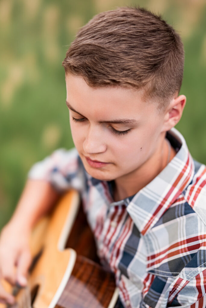 Close-up of teenage boy looking down while playing guitar during a soft, editorial-style musician portrait session in Northern Colorado