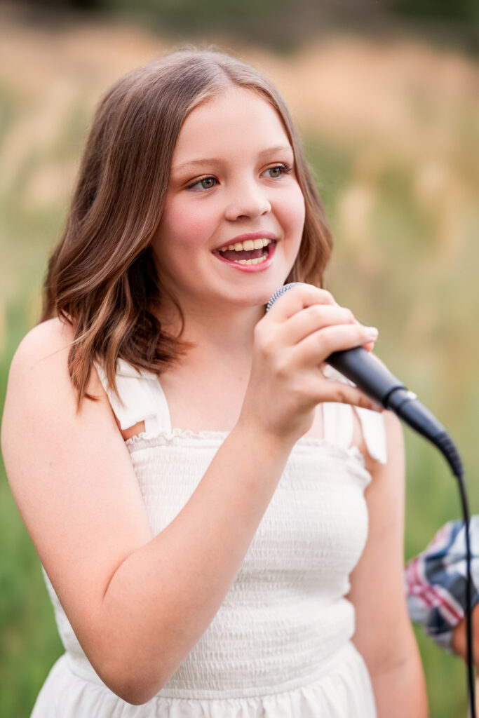 Preteen girl smiling while singing into a microphone during a faith-based musician portrait session in Northern Colorado