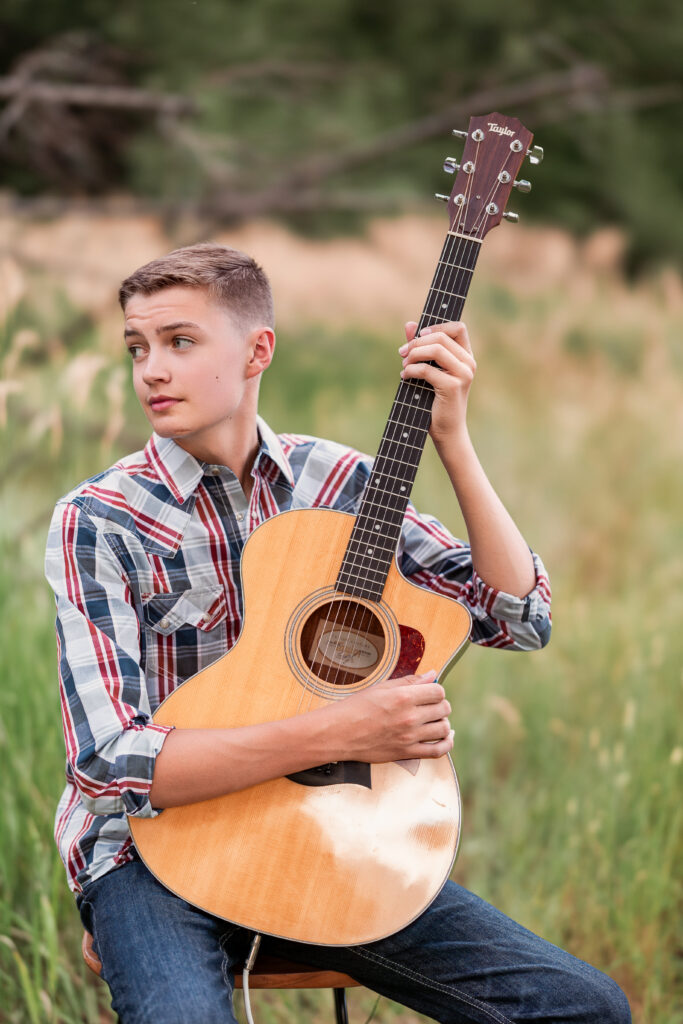 Teenage boy holding acoustic guitar in tall grass field during editorial-style musician portrait session in Northern Colorado