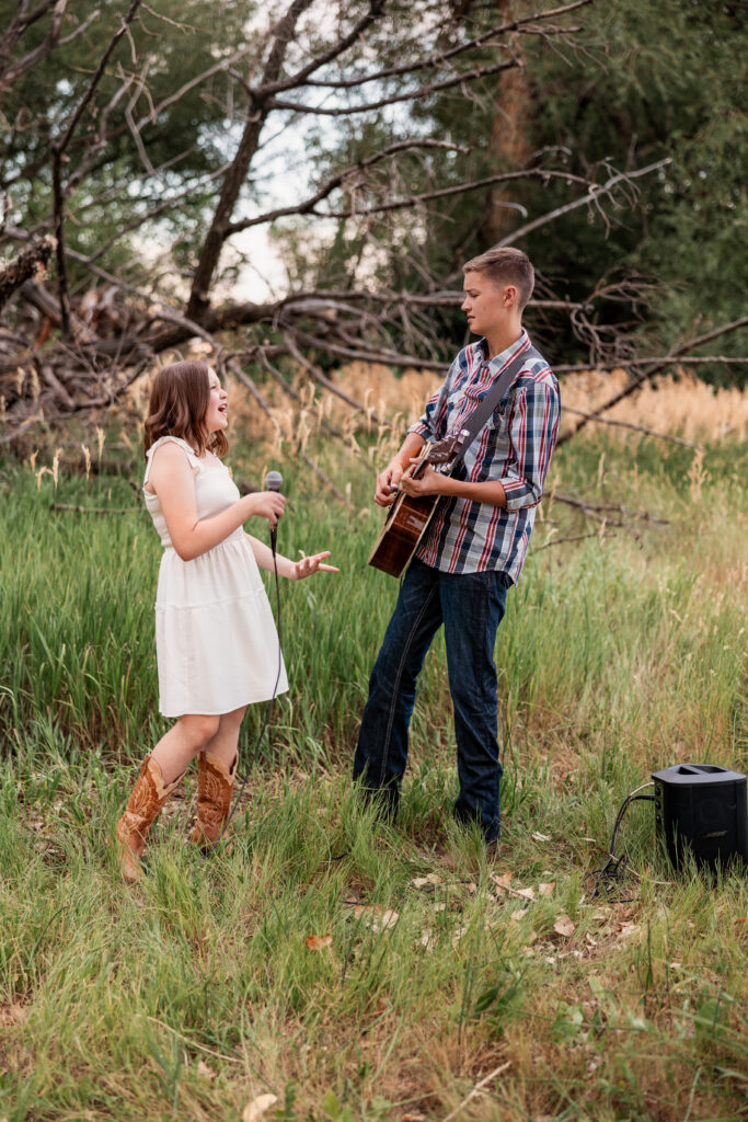 Brother and sister performing outdoors with microphone and guitar in a rustic field during a Northern Colorado country music portrait session