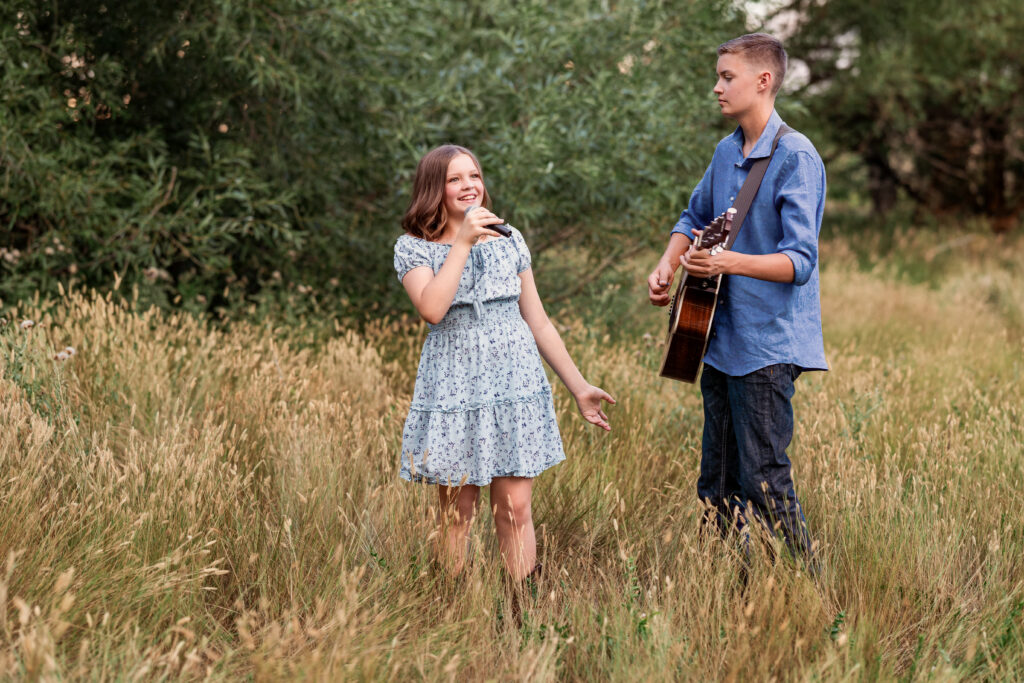 Teenage brother and sister performing together in a tall-grass field with guitar and microphone during a country-Christian portrait session in Northern Colorado
