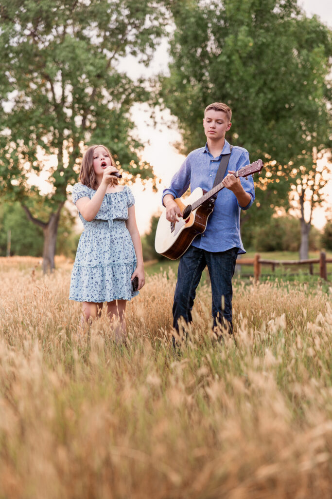 Teen siblings performing at sunset during golden hour in a tall field with guitar and microphone during a Christian country portrait session in Northern Colorado