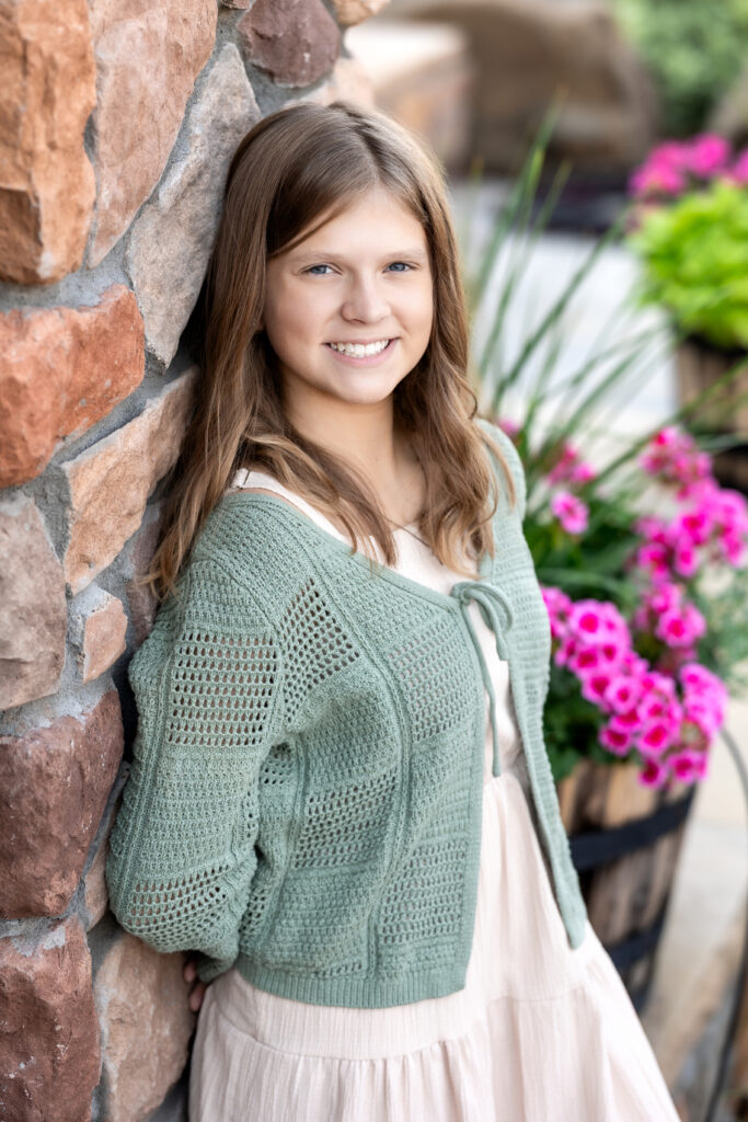 Teen girl smiling against stone wall with pink flowers in back-to-school portrait, Greeley CO