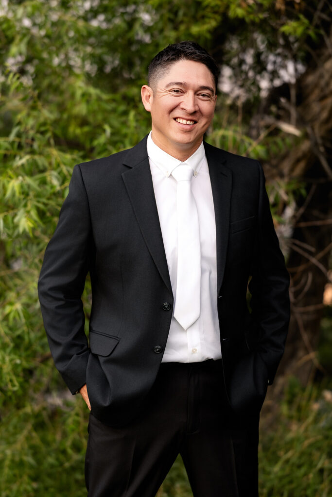 Groom in suit and white tie smiling during his 15-year anniversary portraits at Lions Park in Cheyenne, Wyoming, captured by Heather Lilly Photography.