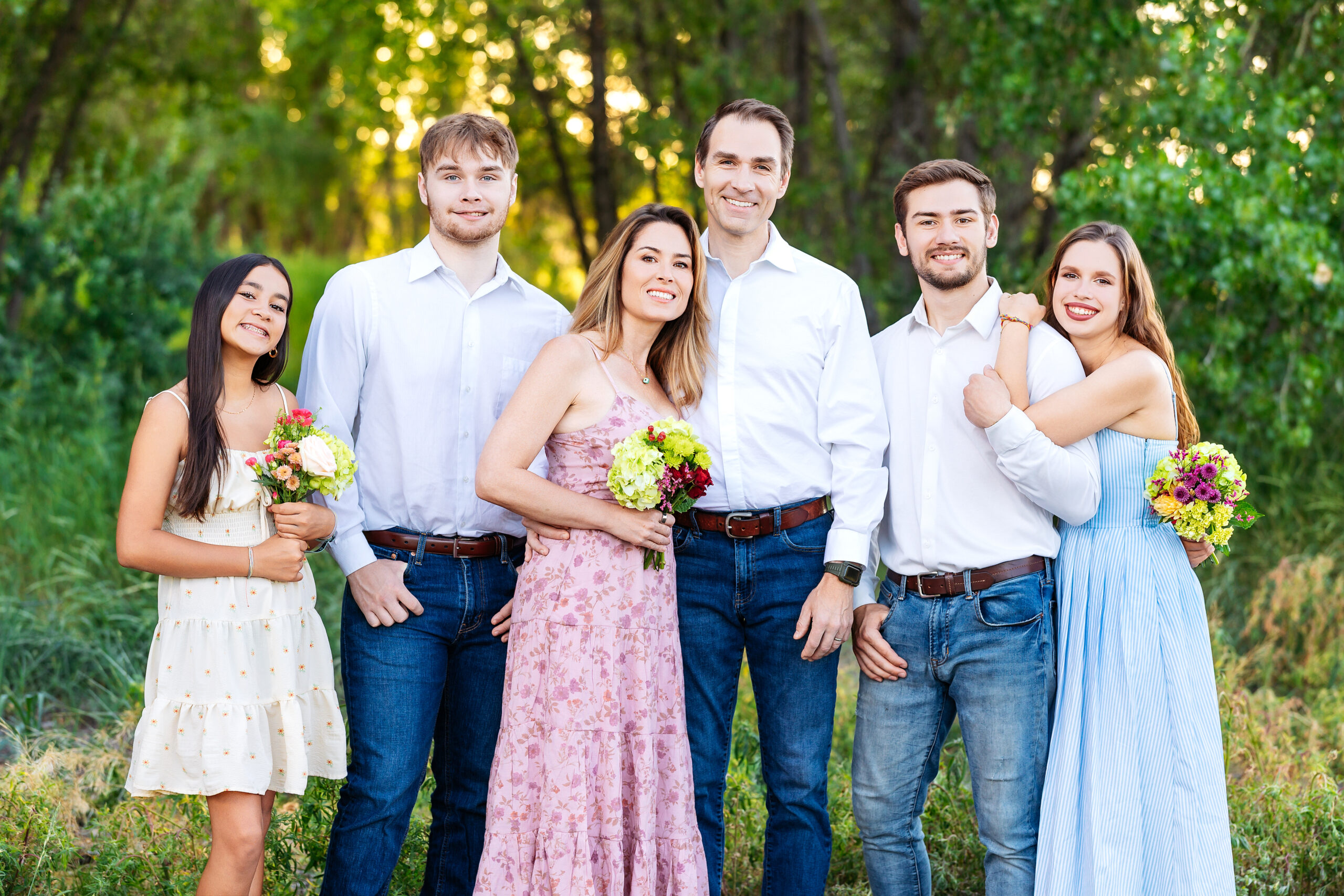 Family of six standing in tall grass at golden hour, dressed in soft summer colors, during a milestone portrait session in Northern Colorado.