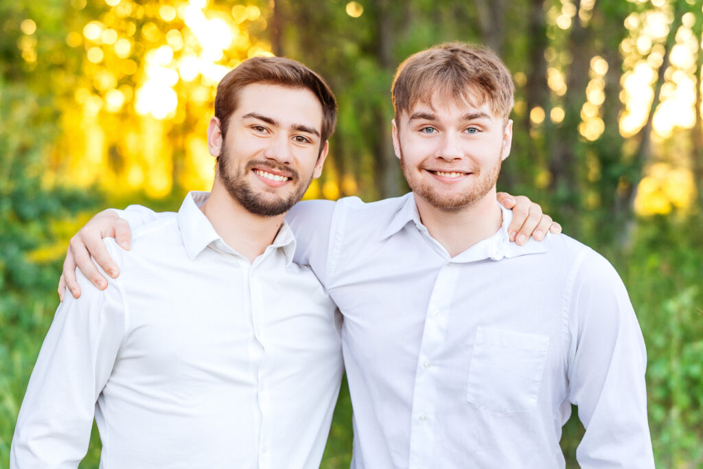 Two brothers standing close with arms around each other, smiling in golden hour light during a family photo session in Northern Colorado.