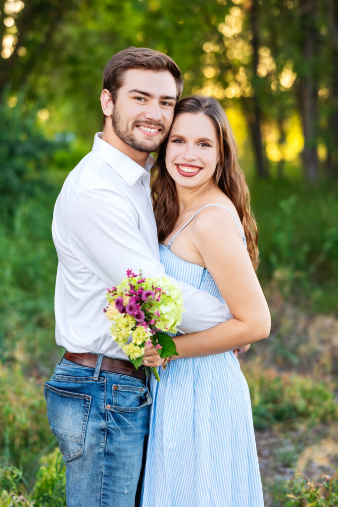 Young couple embracing in a sunlit forest during a Northern Colorado family session, celebrating newlywed joy before beginning a new chapter abroad.