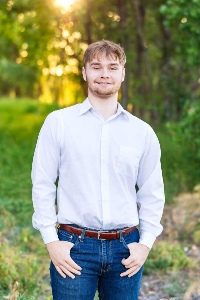 College-aged young man standing in golden hour light wearing a white shirt and jeans during a summer family session in Northern Colorado.