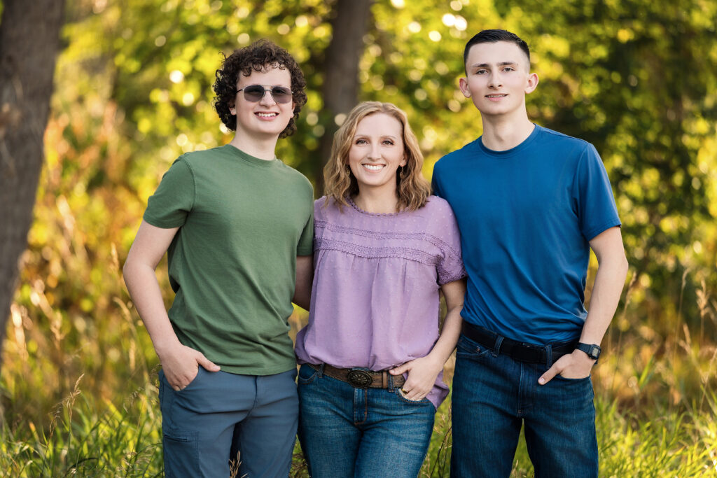 Family standing in tall grass wearing coordinating lavendar, blue and green outfits for their portrait session near Greeley, Colorado with Heather Lilly Photography.