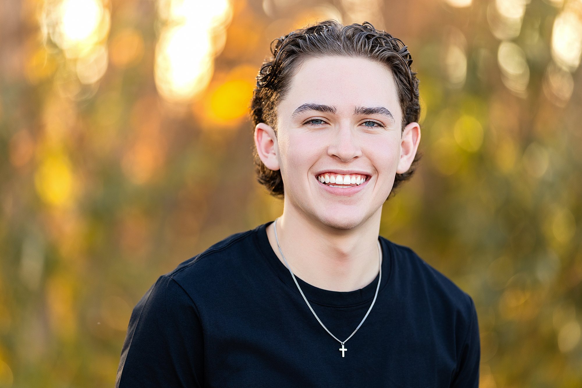 High school senior portrait of a young man in casual fall outfit surrounded by golden leaves, captured by Northern Colorado photographer Heather Lilly.