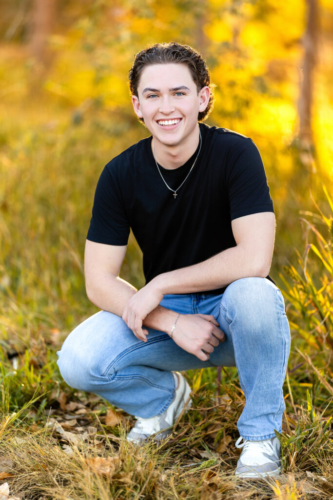 Senior portrait of a young man seated outdoors at golden hour, surrounded by fall color, photographed by Heather Lilly Photography in Northern Colorado.