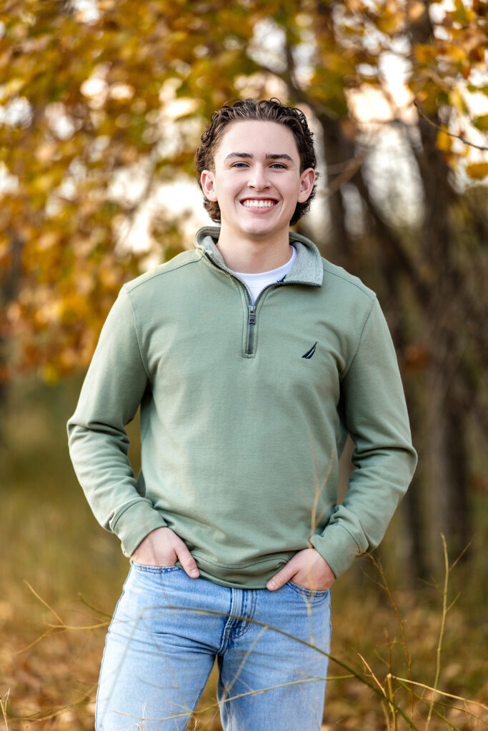 Senior photo of a young man wearing a green pullover against rustic autumn scenery, professional portrait photographer in Colorado.