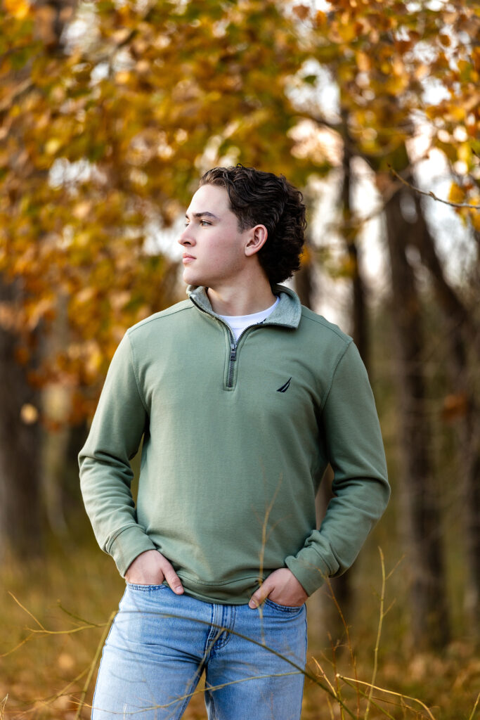 Senior photo of a young man wearing a green pullover against rustic autumn scenery, professional portrait photographer in Colorado.